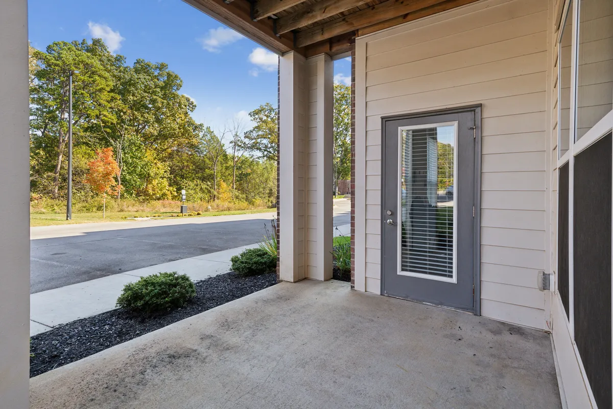 A close-up exterior view of a welcoming front door framed by greenery and a concrete pathway. The scene suggests the comfort of returning home after a day spent exploring the city.