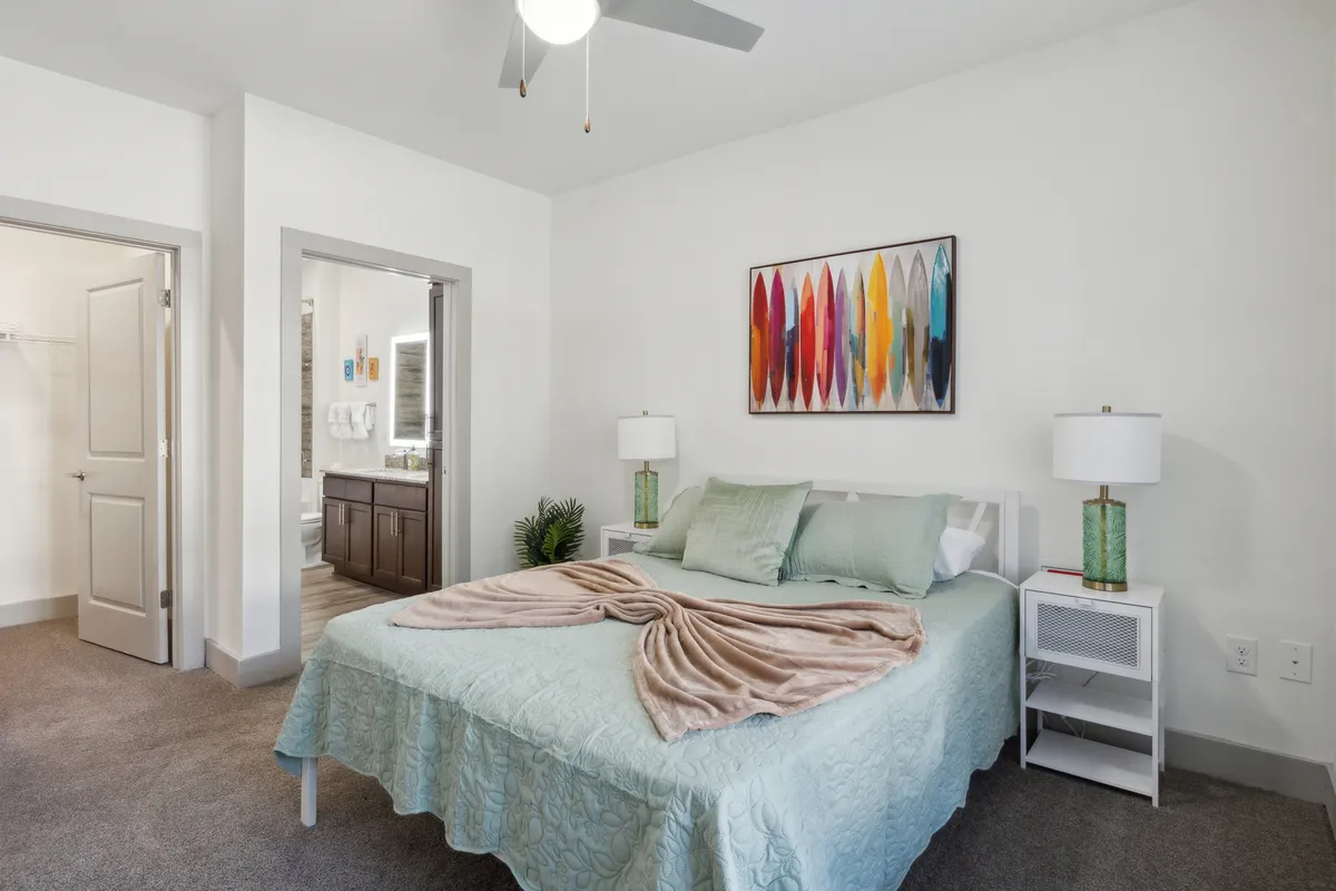 This image showcases a serene bedroom setting with a luxurious bed dressed in light blue premium linens, colorful wall art above the headboard, and matching nightstands with glowing lamps on each side. The overall mood is calm and cozy, ideal for rest and relaxation.