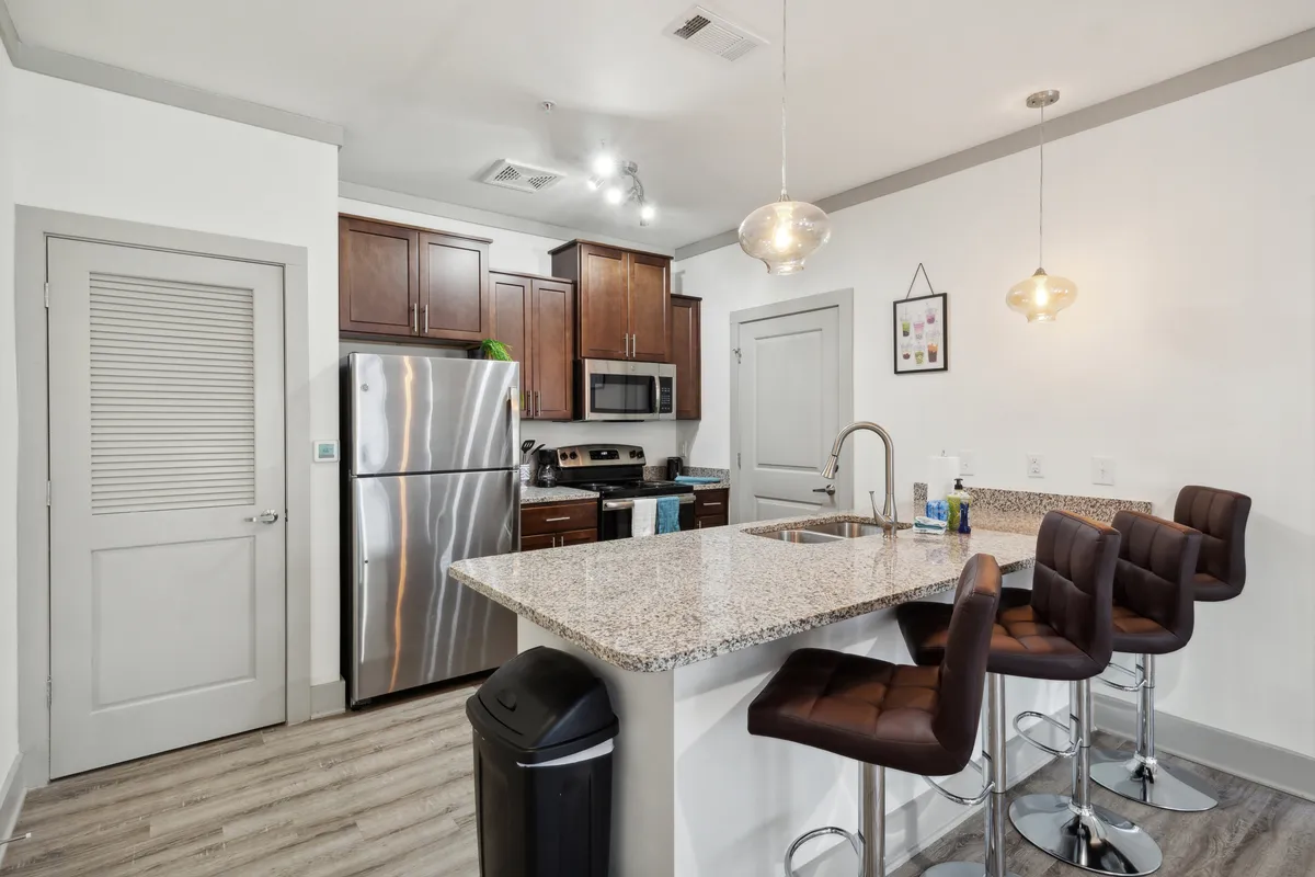 A modern kitchen with a granite countertop, stainless steel appliances, and bar stools at the breakfast bar. The layout is welcoming, perfect for both cooking and casual dining or entertaining guests.