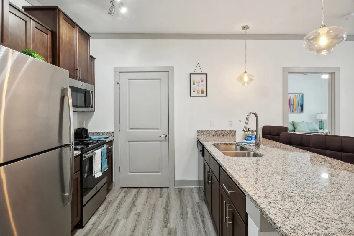 A contemporary kitchen scene featuring a granite countertop, stainless steel appliances, striking pendant light fixtures, and stylish wall art. The atmosphere is both modern and welcoming, suitable for hosting or enjoying a quiet meal.