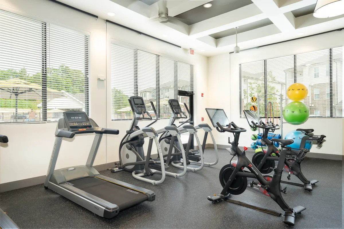 A well-equipped fitness center interior with modern treadmills, elliptical machines, stationary bikes, and exercise balls. The space is bright and motivating, set up for both individual and group workouts, reflecting a sense of wellness and community.